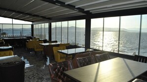 Ein Restaurant mit Tischen und Stühlen, große Fenster mit Blick auf ein Gewässer.