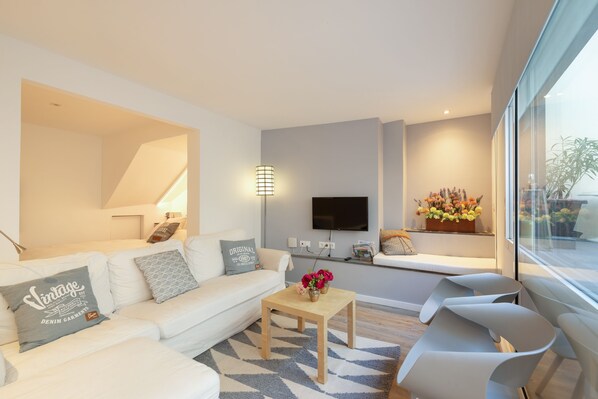 A modern living room with a white sofa, a wooden coffee table, and a flat-screen TV mounted on the wall. - OLD TOWN Apartment With Interior Terrace - Barreirinha (Funchal)