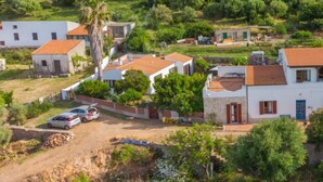 Área residencial com casas de paredes brancas e telhados de telha vermelha, cercada por vegetação e árvores.