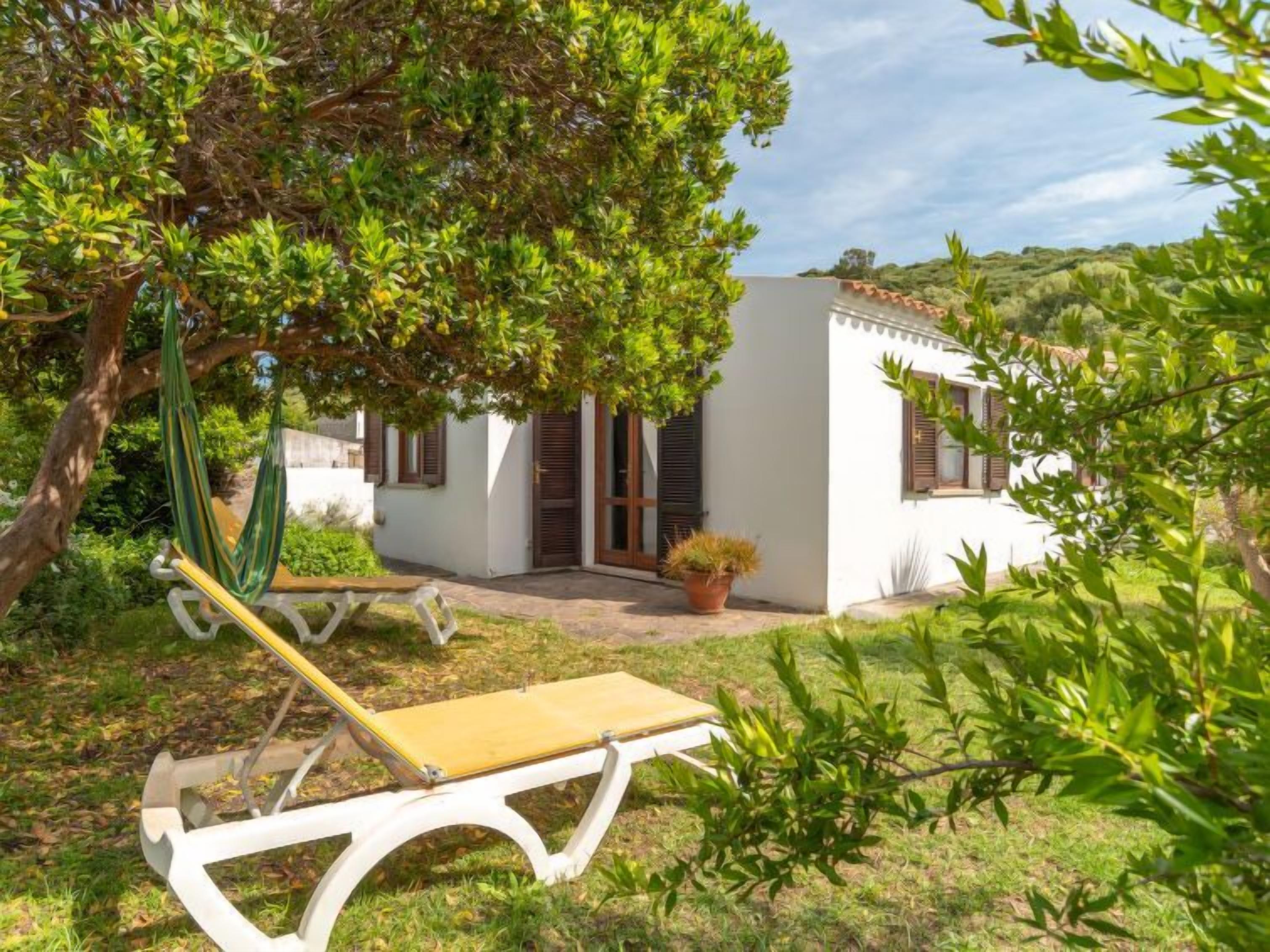 A white villa with a small patio, a hammock, and a sun lounger.