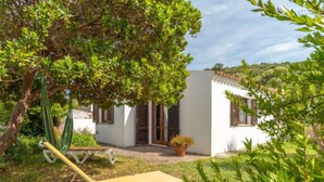 Uma vila branca com um pequeno alpendre, uma rede e uma espreguiçadeira.