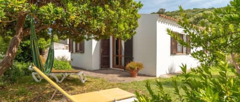 Una villa blanca con un pequeño patio, una hamaca y una tumbona.