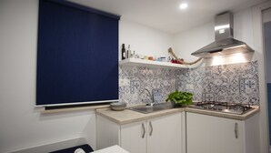 A compact kitchen with a gas stove, a sink, and a window with a blue blind. - The Holy Mary inside (Tropea)