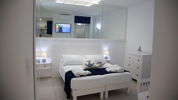A bedroom with a large bed, bedside tables with lamps, a TV, and a mirror. - The Holy Mary inside (Tropea)
