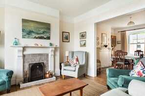 A living room with a fireplace, a dining area with a table and chairs, and a hallway leading to another room. - Captains Cottage - Four Bedroom Cottage, Sleeps 7 (St Mawes)