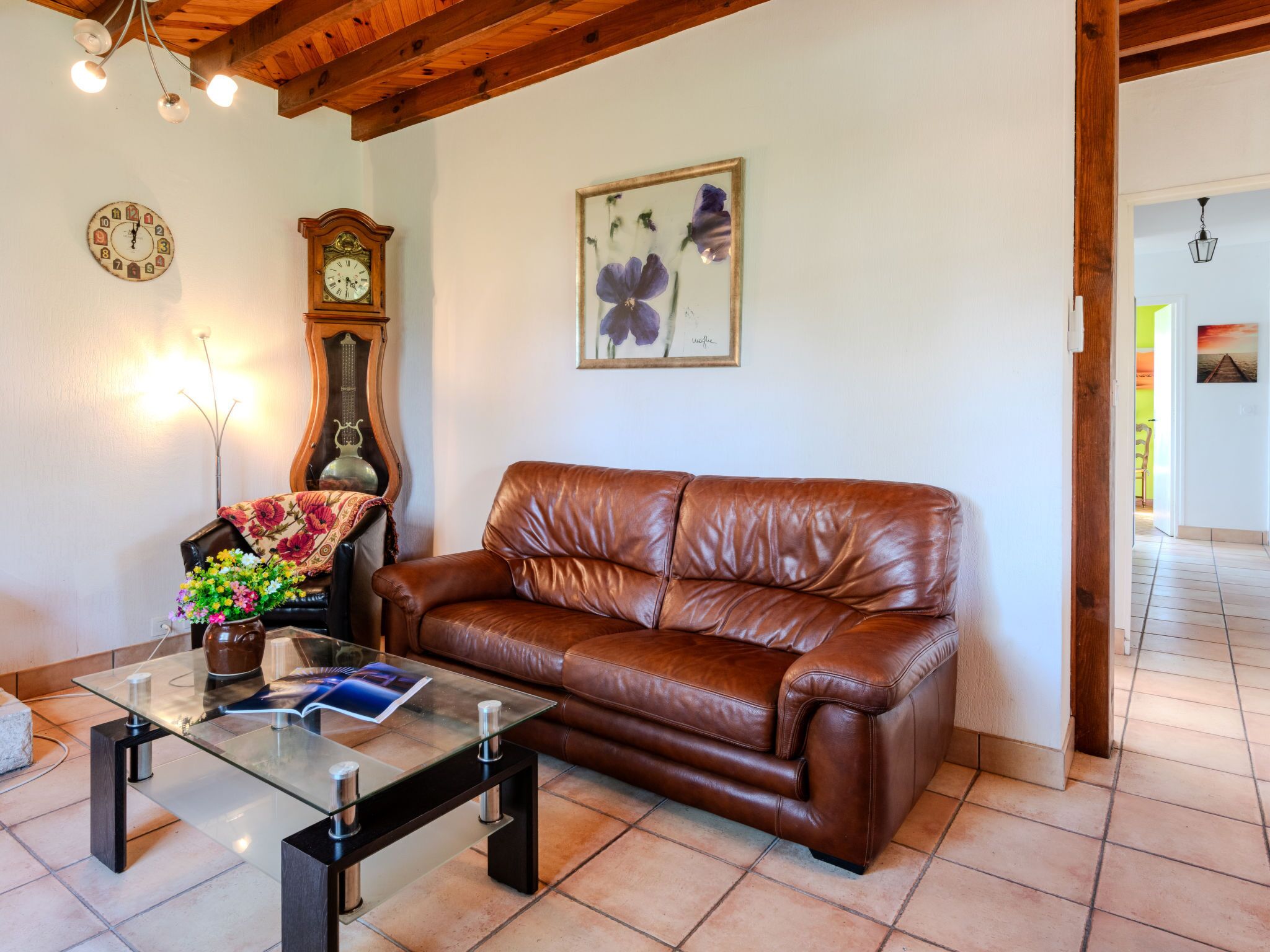 Un soggiorno con un divano in pelle marrone, un tavolino in vetro, una sveglia, un quadro floreale e un soffitto in legno.