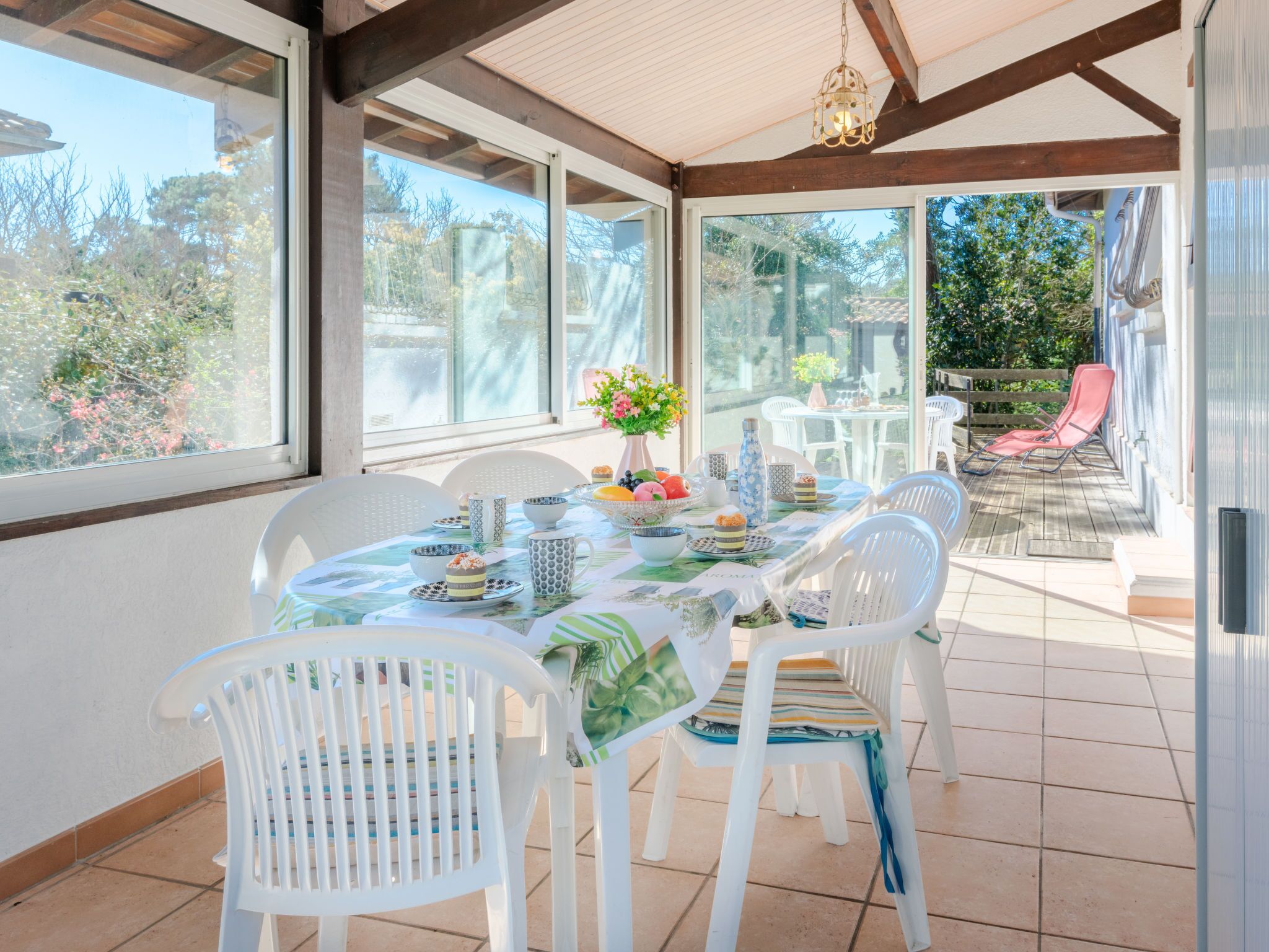 Un patio soleado con una mesa lista para el té, rodeado de sillas blancas y vistas al jardín.