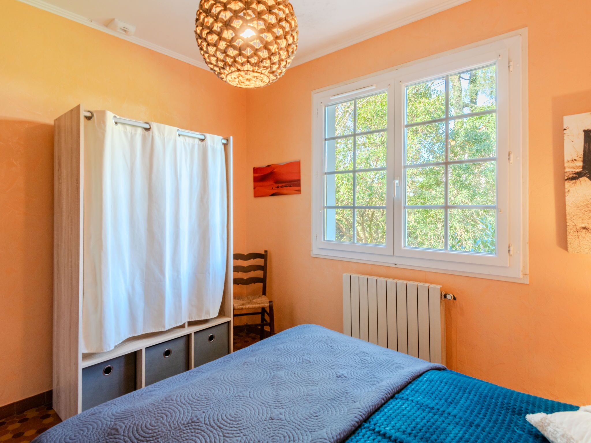 A bedroom with a bed, a window, a radiator, a chair, and a towel rack.