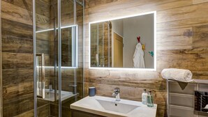 Ein modernes Badezimmer mit Duschkabine aus Glas, einem großen Spiegel und einem Waschtisch mit Spüle und Pflegeprodukten.