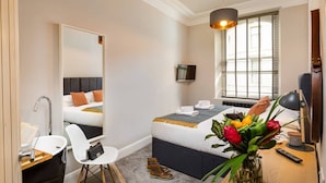 Ein Hotelzimmer mit Bett, Nachttisch, Stuhl, Schreibtisch und einem großen Spiegel.