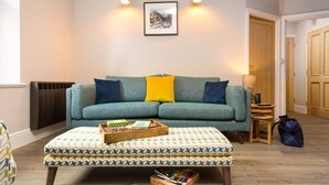 Ein gemütliches Wohnzimmer mit einem türkisfarbenen Sofa, einem gemusterten Hocker und einem gerahmten Bild an der Wand.
