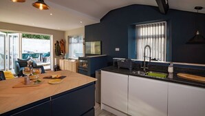 Une cuisine moderne dotée d’un îlot central, de meubles blancs et d’un plan de travail noir. On y trouve une fenêtre avec des stores, un évier et un coin repas avec une table et des chaises.