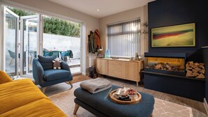 Un salon moderne avec un canapé, une table basse sur laquelle est posé un plateau, une cheminée et une grande fenêtre avec des rideaux.