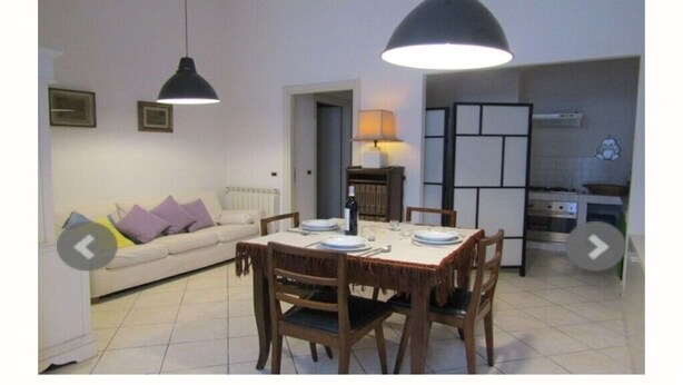 Een eethoek met een tafel voor vier personen, een bank met kussens, en een keuken op de achtergrond.