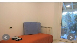 Een kleine slaapkamer met een enkel bed, een radiator en een schuifdeur naar een buitenruimte.