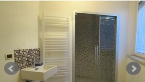 Een badkamer met een wit wastafelmeubel, een betegelde spatwand, een douchecabine met glazen wanden en een witte handdoekhouder.