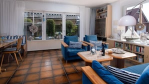 Una sala de estar moderna con piso de baldosas, sofás azules, una mesa de centro de madera y una estantería.
