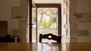 Ein Blick ins Zimmerinnere zeigt einen Holztisch, einen Stuhl, eine Steinsäule und eine Tür, die nach draußen führt.