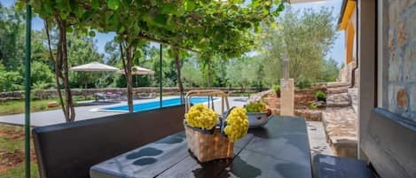 Un patio al aire libre con una mesa de piedra, dos bancos y una cesta de flores amarillas.