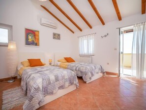 A room with two beds, a radiator, a window with curtains, and a ceiling with wooden beams. - Vacation home Mila by Interhome (Krk/Dobrinj)