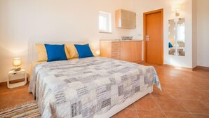 Een slaapkamer met een bed, nachtkastje, raam, spiegel en deur.
