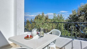 A balcony with a table set for two, a chair, and a view of trees and a clear sky. - Apartment Rubin by Interhome (Hvar/Pokrivenik)
