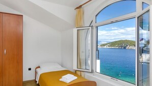 A bedroom with a bed, a wooden wardrobe, and a window with a view of the sea and a hilly landscape. - Apartment Rubin by Interhome (Hvar/Pokrivenik)