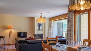 A modern living room with a sofa, dining table, chairs, a TV, and a fireplace. - Dents Rousses B4 by Interhome (Siviez-Nendaz)