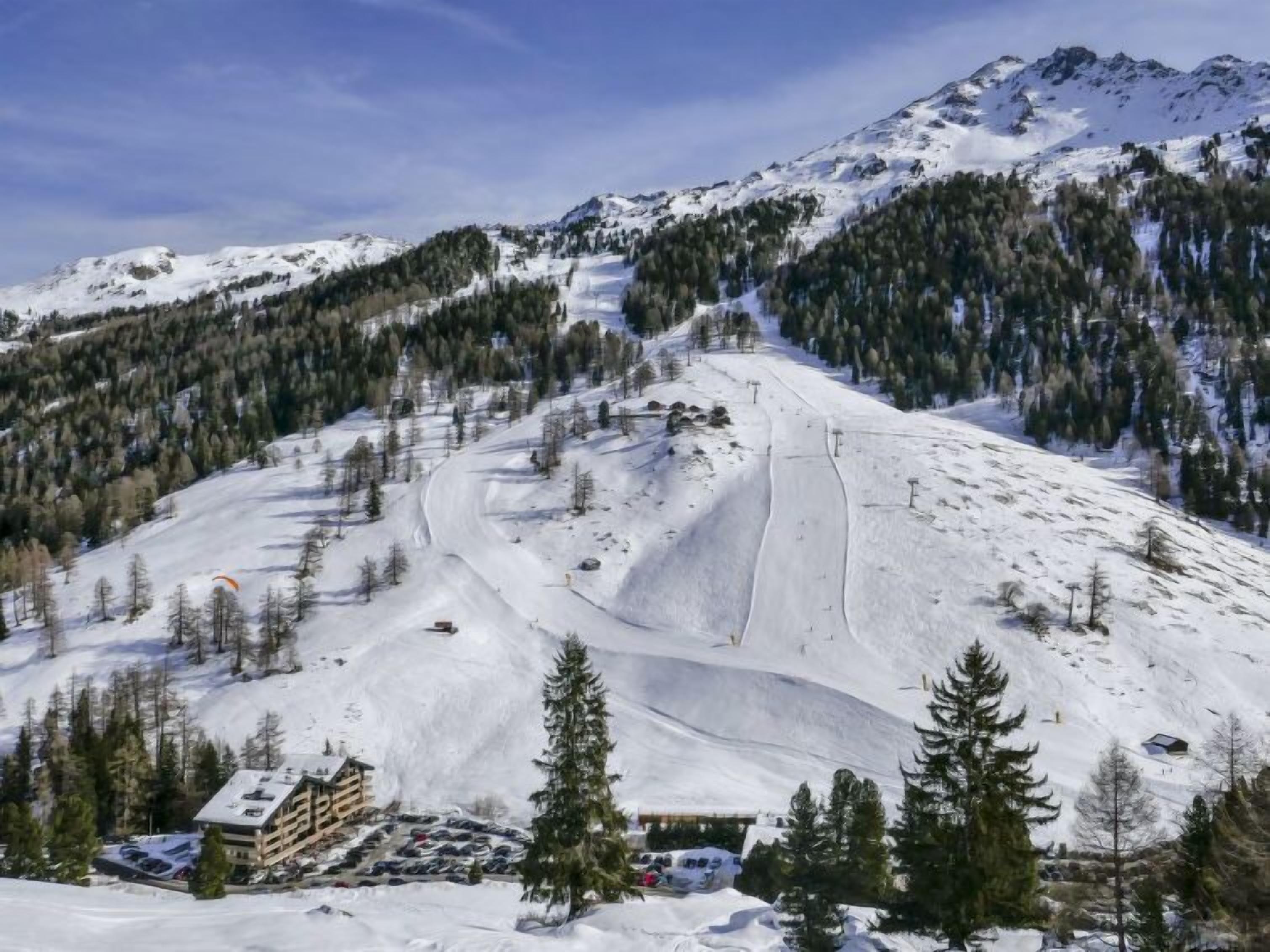 A snow-covered ski resort with a building, parking area, and ski slopes.