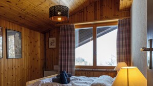 A wooden room with a bed, a lamp, and a window with curtains. - Dents Rousses B4 by Interhome (Siviez-Nendaz)