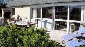 Une maison moderne dotée d’un patio comprenant une table à manger, des chaises et un barbecue.