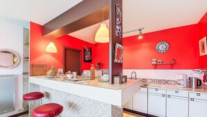 Une cuisine avec des murs rouges, des meubles blancs et deux tabourets de bar rouges.