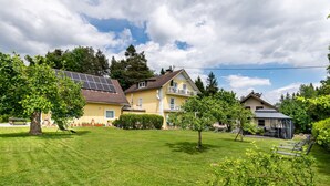 Ein gelbes Gebäude mit geneigtem Dach, umgeben von einem gepflegten Rasen und Bäumen.