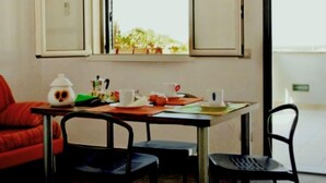 A room with a table, chairs, a window with a view of greenery, and a red chair. - Cava Larica by Interhome (Scicli)