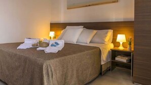 A neatly made bed with white linens, two bedside tables with lamps, and a wall-mounted artwork above the bed. - Cava Larica by Interhome (Scicli)