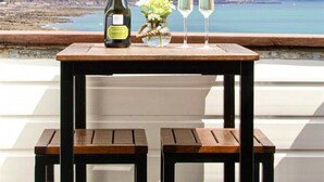 A table with a bottle and two glasses on a balcony overlooking a coastal landscape. - Emelle - Three Bedroom Cottage, Sleeps 7 (Kingsand)