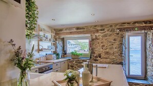 A modern kitchen with stone walls, a large island, and a view of the sea. - Emelle - Three Bedroom Cottage, Sleeps 7 (Kingsand)