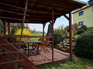 A wooden deck with a table and chairs, overlooking a green landscape and a building. - Jesenný by Interhome (Tanvald)
