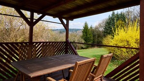 Un espace extérieur aménagé, abrité et doté d’une table et de chaises, offrant une vue sur un paysage verdoyant et des arbres.