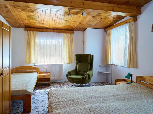 A bedroom with two beds, a green armchair, wooden ceiling, and large windows with curtains. - Jesenný by Interhome (Tanvald)