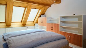 Une chambre avec un plafond en pente, des fenêtres de toit, un lit avec une literie à motifs, une armoire en bois et un radiateur blanc.