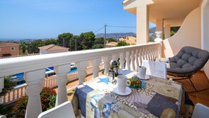 Un balcón con una mesa para dos, una silla y vistas al mar y al paisaje urbano.