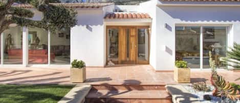 A modern house with a tiled roof, a front entrance with a wooden door, and a small garden area with steps leading to the door.