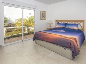A bedroom with a bed, a nightstand, a lamp, and a view of a garden through a sliding door.