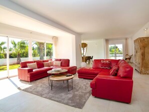 A spacious living room with a red sectional sofa, a coffee table, and large windows offering a view of the outdoors.