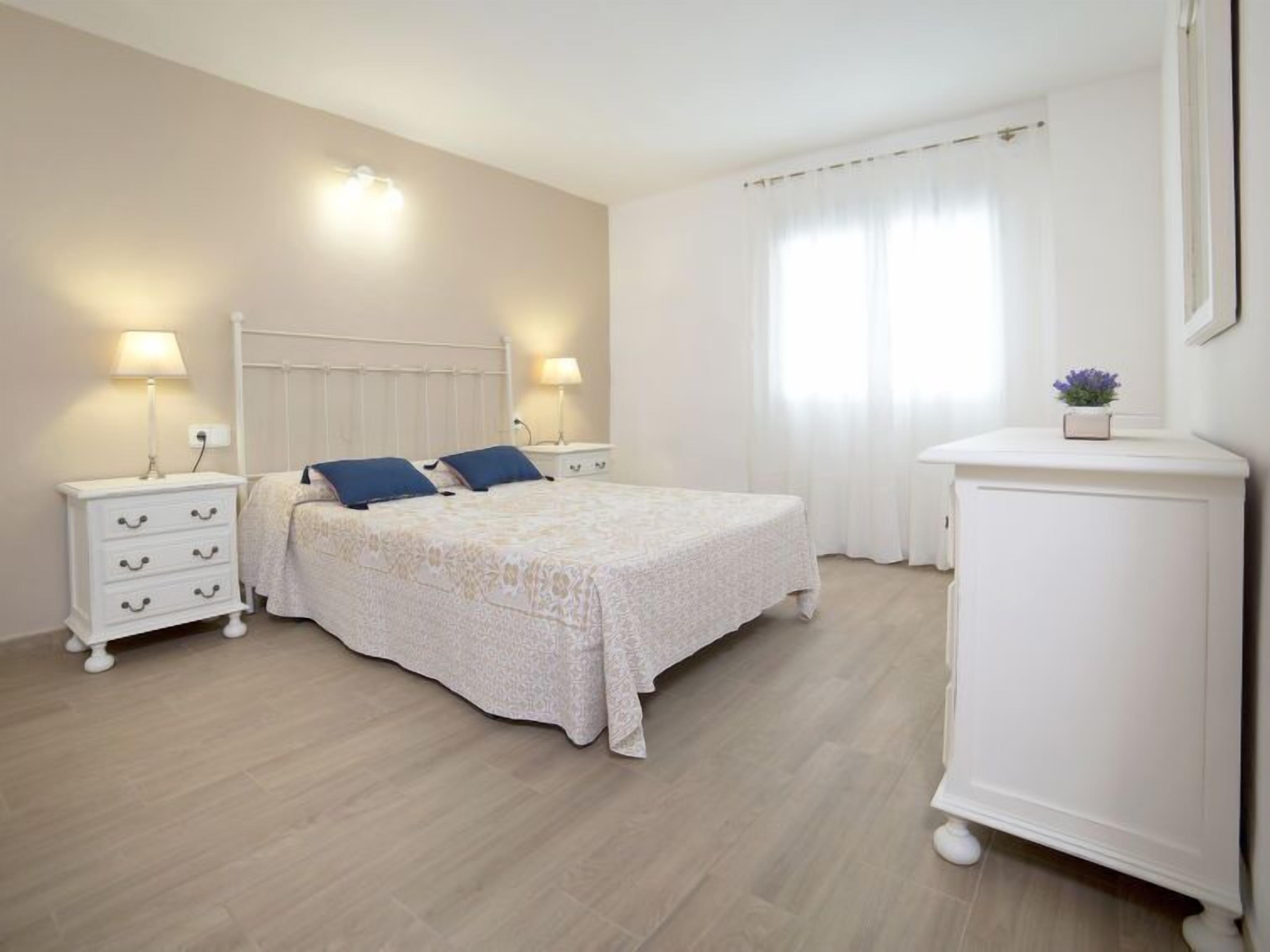 A bedroom with a bed, two bedside tables, a nightstand, a cabinet, and a window with curtains.