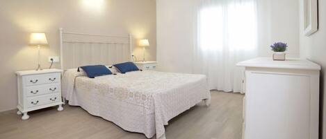 A bedroom with a bed, two bedside tables, a nightstand, a cabinet, and a window with curtains.