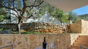 A table set for two with a bottle of wine, glasses, and plates, set against a stone wall with a tree and a stone staircase. - Apartment Cico by Interhome (Hvar/Pokrivenik)