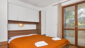 A bedroom with a bed, white cabinets, a wooden headboard, a wall-mounted light, and a sliding glass door to the outside. - Apartment Cico by Interhome (Hvar/Pokrivenik)