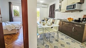 A compact kitchen with a microwave, stove, and a dining area with a table and chairs. - Aquanur by Interhome (Vodice/Tribunj)